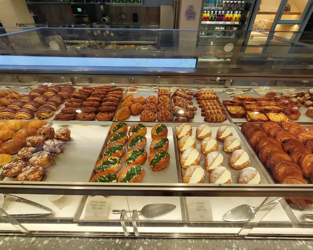 A display case filled with various pastries: croissants, filled rolls, and decorated buns. The arrangement is colorful and inviting, evoking warmth and indulgence.