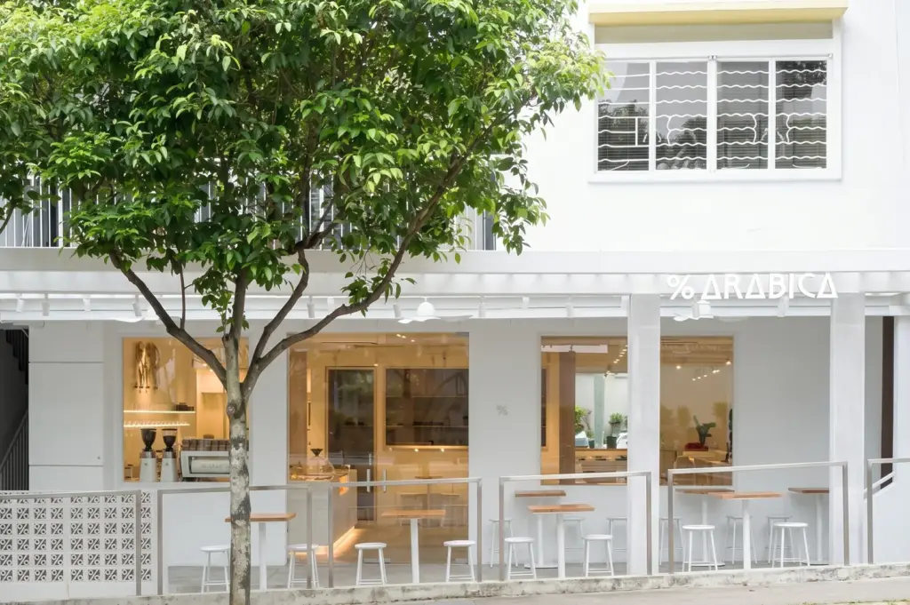Exterior view of the %Arabica coffee shop in Chip Bee Gardens, featuring the brand's signature minimalist white facade, large windows, and outdoor seating area.