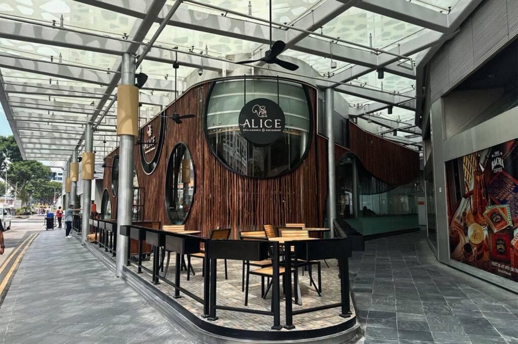 Unique "Alice" restaurant building with a curved, woven bamboo exterior and dark outdoor dining tables under a glass canopy.