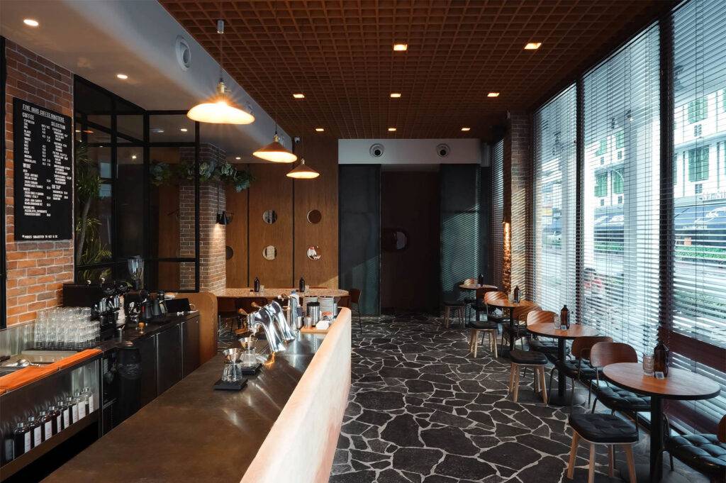 Dark, industrial-style cafe with a mosaic stone floor, exposed brick, wood-paneled ceiling, and small round tables near the windows.
