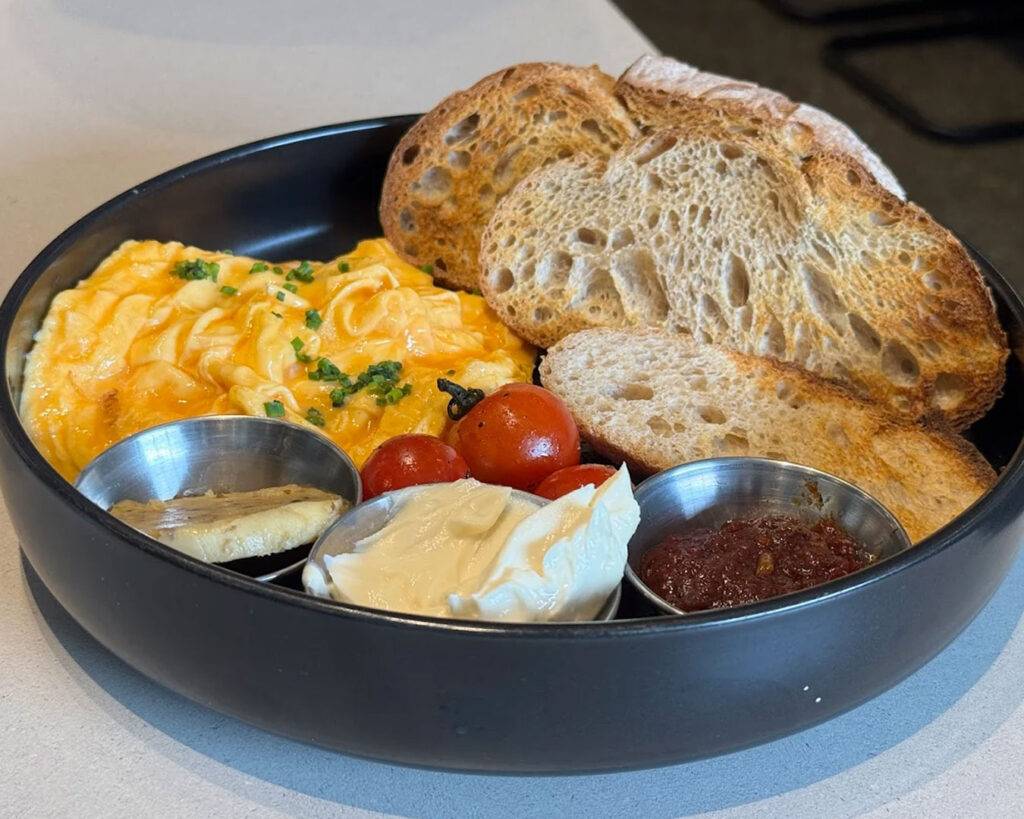 A beautifully plated breakfast of toasted artisan bread topped with softly cooked eggs, served in a warm café setting with natural light.