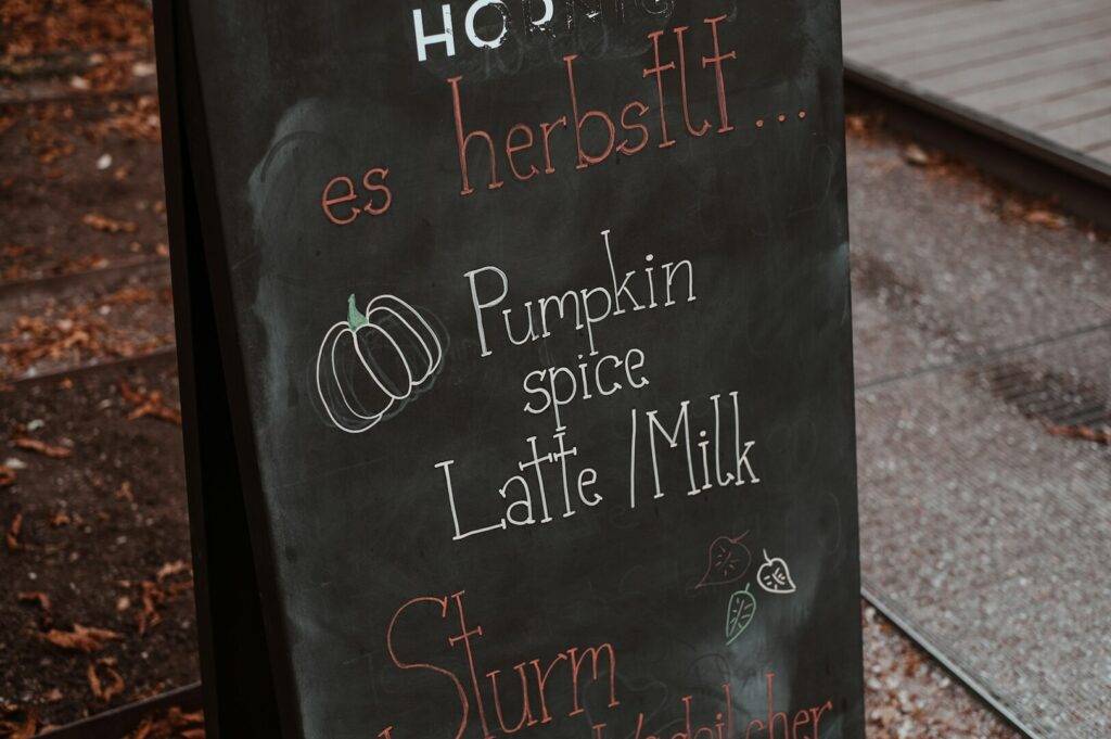 A chalkboard coffee menu advertising Pumpkin spice Latte/Milk outside a coffee shop.