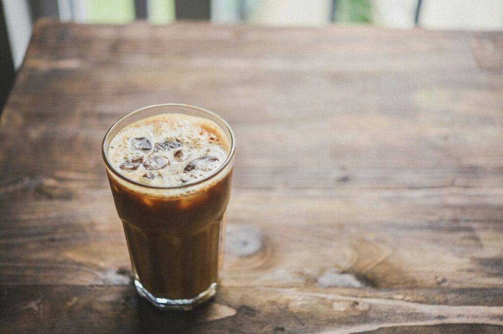 A refreshing iced coffee placed on a wooden table, showcasing its rich color.
