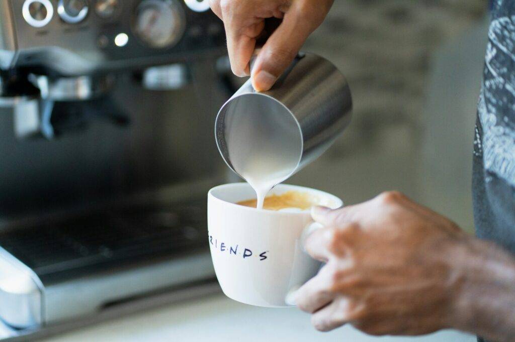 A person pouring coffee with milk into a cup, showcasing the rich blend of colors and textures.