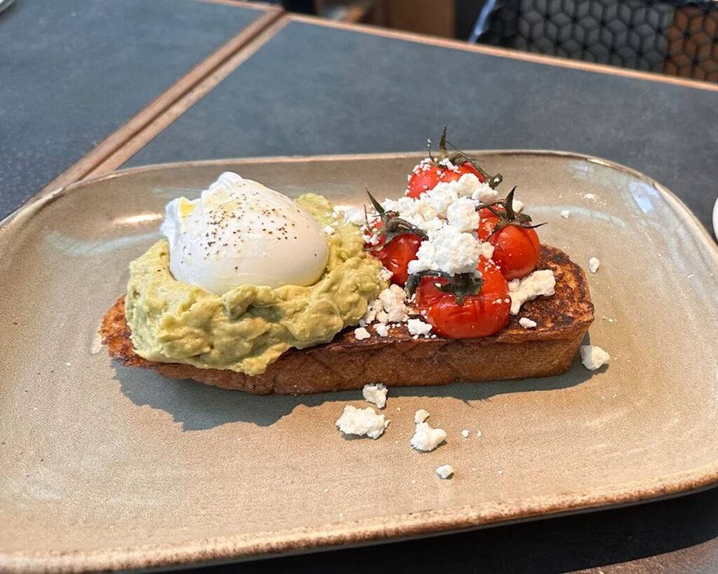 A rich breakfast dish combining soft burrata cheese, crisp bacon, and toasted sourdough, balancing indulgence with simplicity.