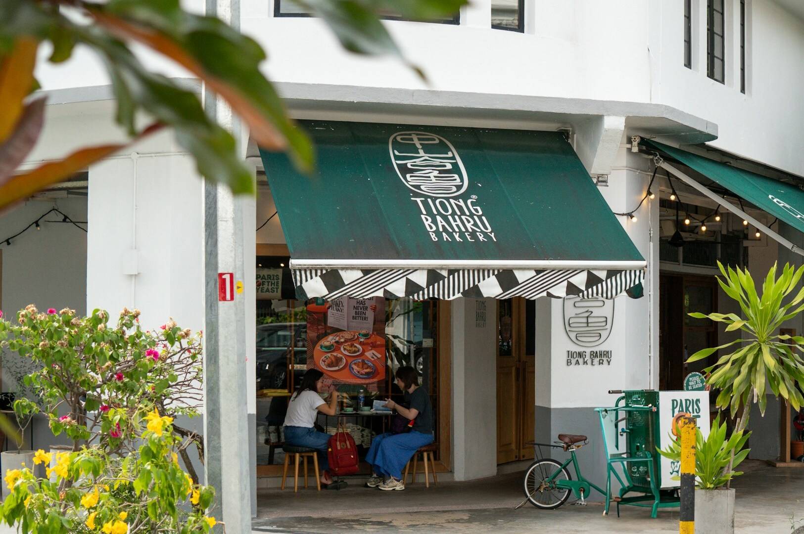 A cafe named Tiong Bahru Bakery with a green awning and a bicycle parked in front.