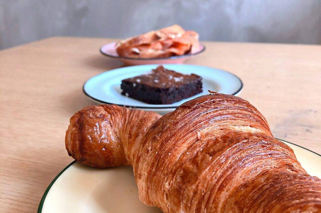 A Tiong Bahru croissant and a slice of cake elegantly arranged on a white plate.