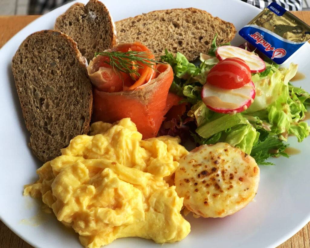 Luxurious truffle-infused scrambled eggs paired with French toast topped with glossy stout-glazed bacon, blending savoury depth with subtle sweetness.