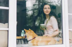 Inside a Puppy Cafe, a woman relaxes on a window sill with a dog, creating a warm and inviting scene.