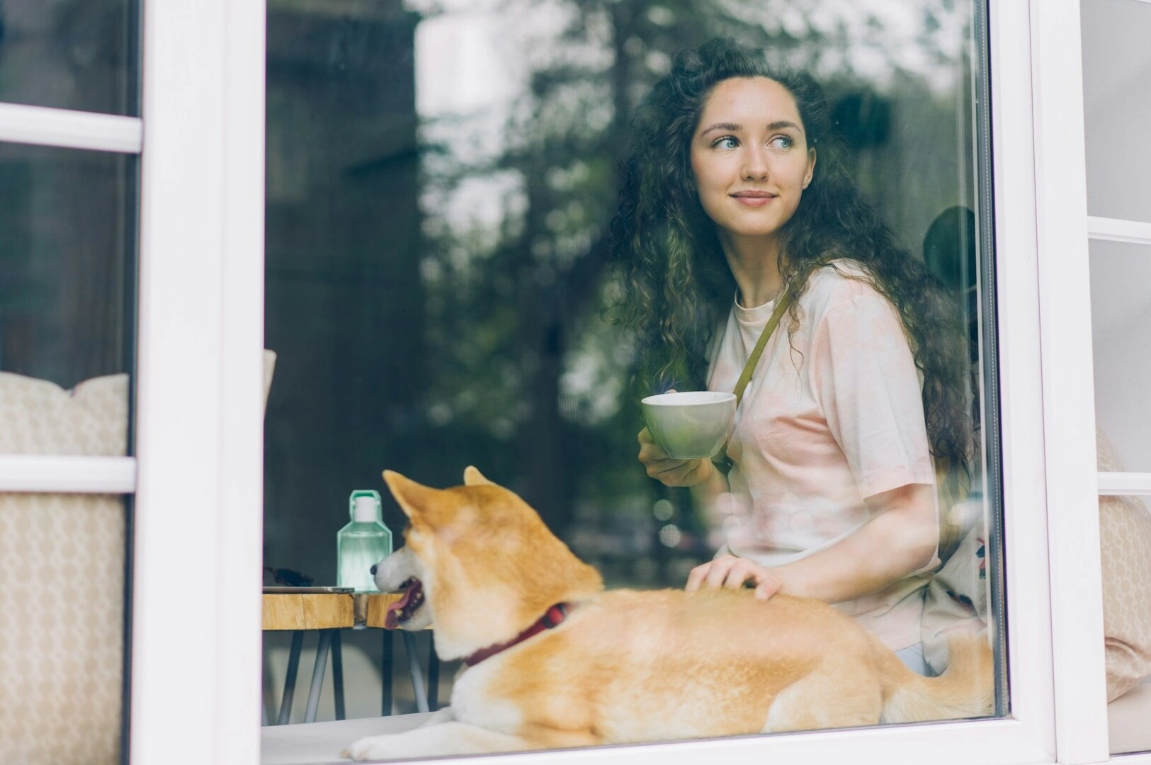 Inside a Puppy Cafe, a woman relaxes on a window sill with a dog, creating a warm and inviting scene.
