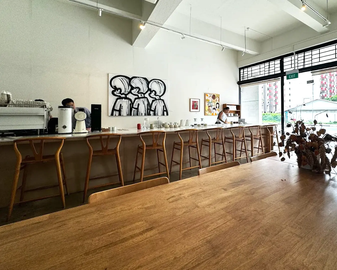 Spacious café interior with wooden furniture, barista at counter, and modern art on walls. Bright light and a cozy, inviting atmosphere.