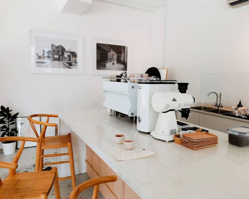 A minimalist café interior with a sleek espresso machine on a wooden counter, surrounded by warm lighting and clean, neutral décor that creates a calm and modern coffee-drinking atmosphere.