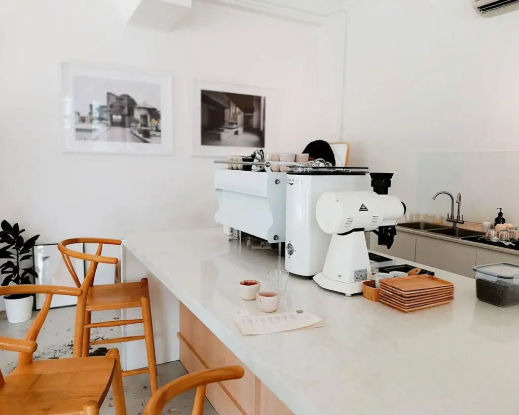 A minimalist café interior with a sleek espresso machine on a wooden counter, surrounded by warm lighting and clean, neutral décor that creates a calm and modern coffee-drinking atmosphere.