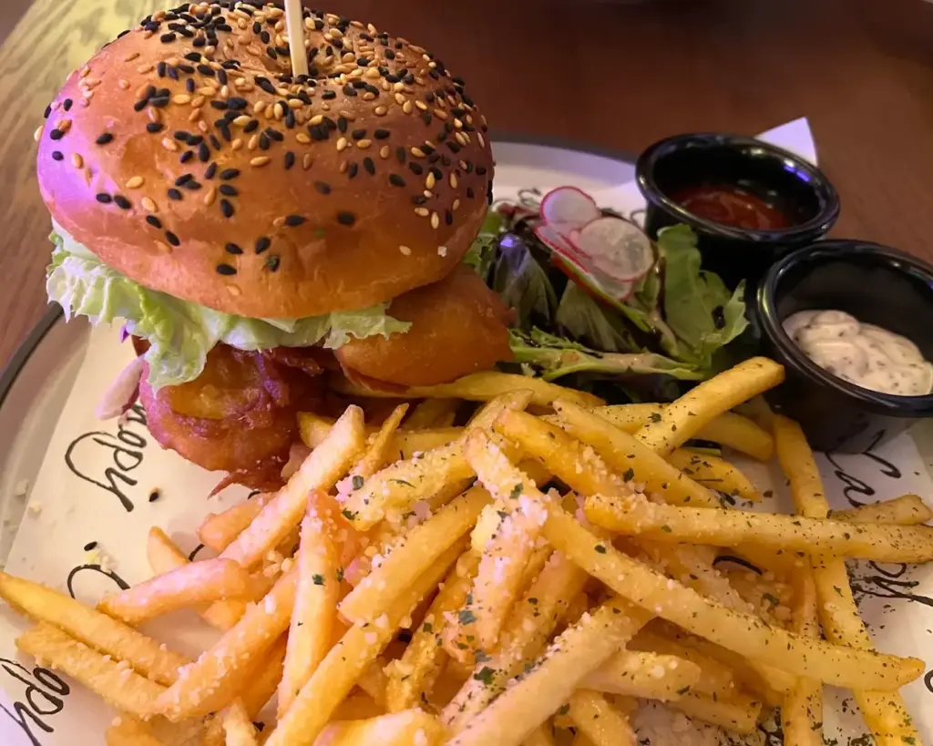 A freshly prepared burger served on a plate with a side of golden, crispy fries. The burger features a soft bun layered with a juicy patty and fillings, creating a hearty and satisfying meal.