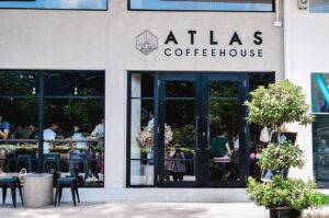 Atlas Coffeehouse exterior view with large glass windows showing customers inside and a potted plant outside.