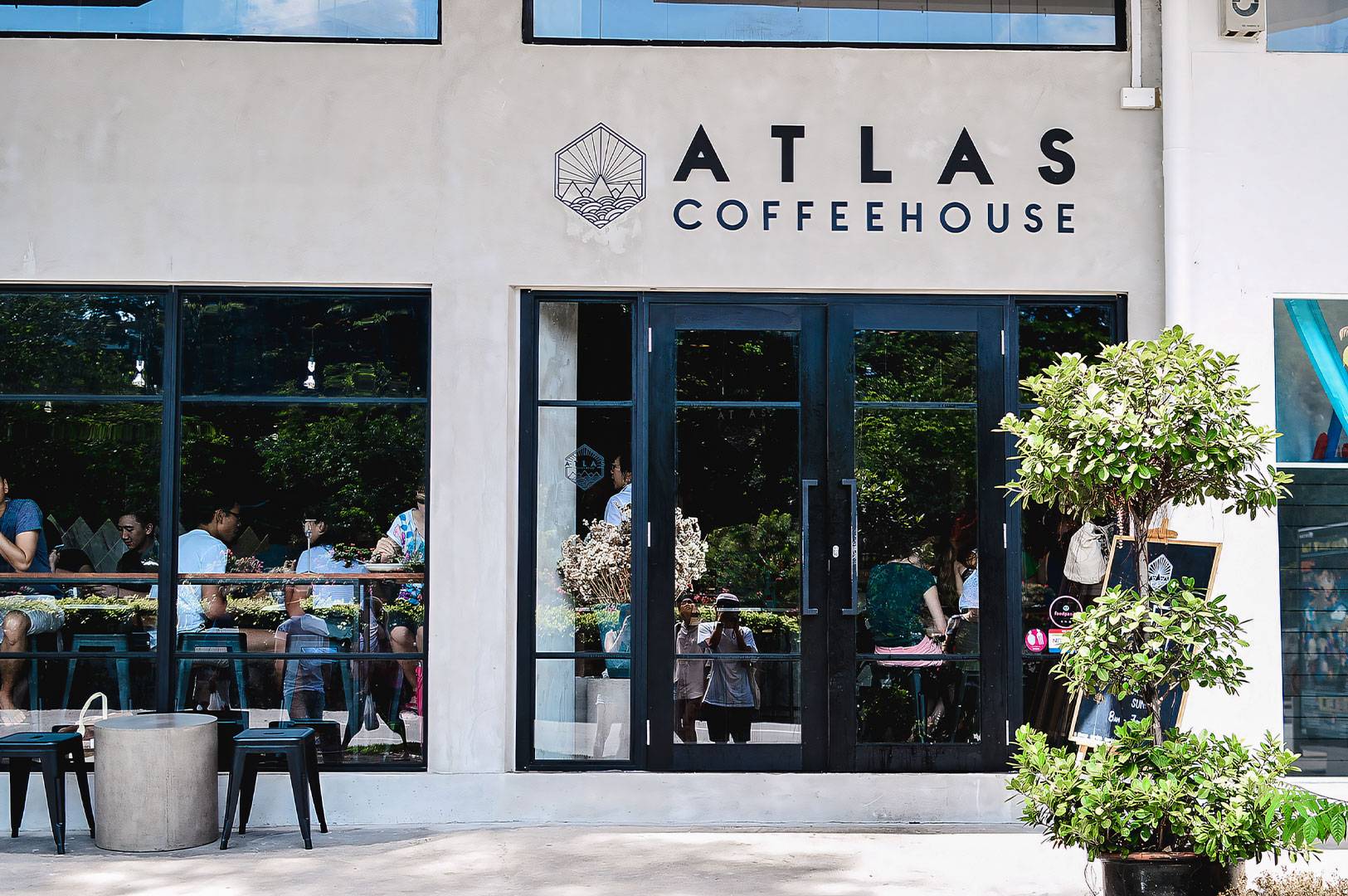 Atlas Coffeehouse exterior view with large glass windows showing customers inside and a potted plant outside.