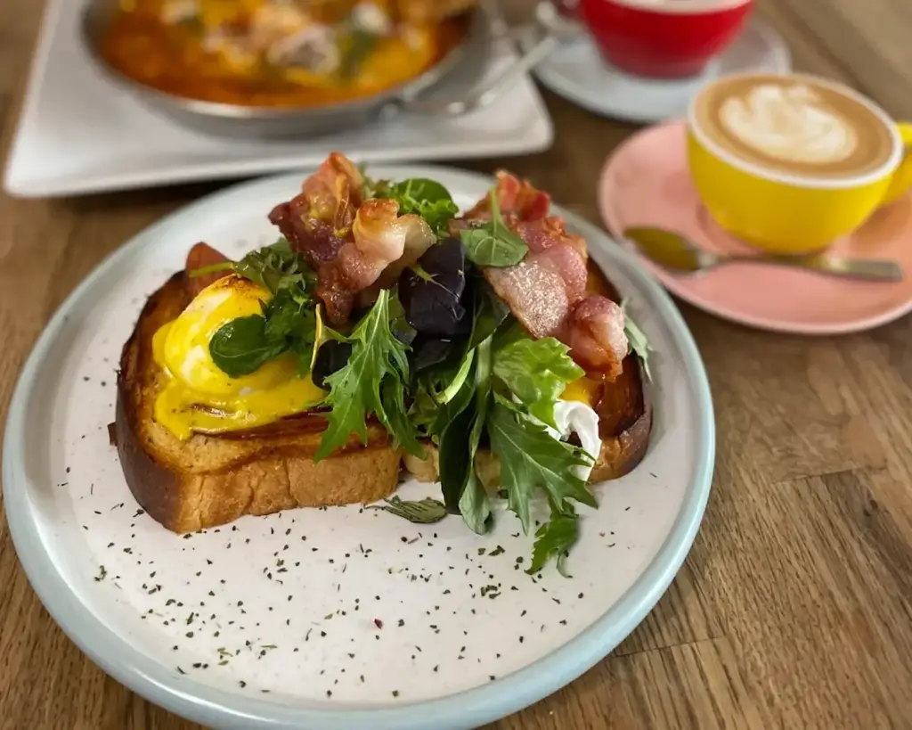 A slice of toasted bread topped with crispy bacon, a perfectly cooked egg, and a fresh side of salad. The combination offers a balance of savoury richness and light, crisp greens.