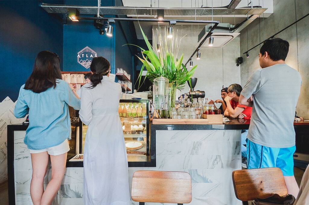 Interior view of Atlas Coffeehouse counter, showing two women ordering and customers seated at a table.