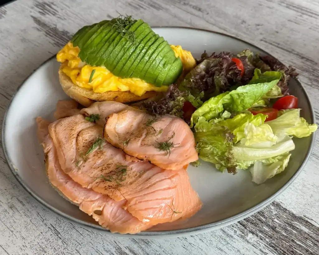 A wholesome plate of fresh salad paired with grilled salmon, alongside a slice of toasted bread topped with egg and avocado. The dish highlights a nutritious mix of protein, healthy fats, and vibrant greens.