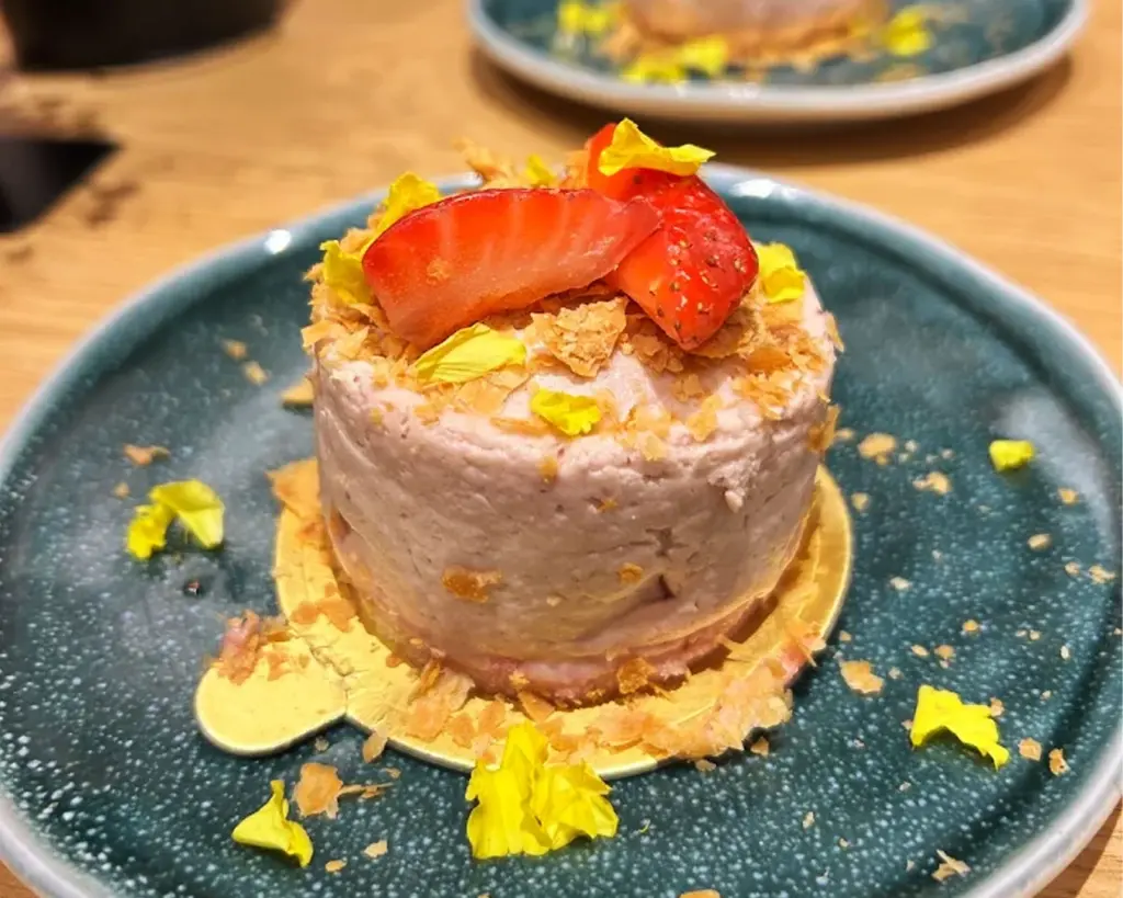 An elegantly plated dessert garnished with fresh strawberries and edible flowers, arranged delicately to create a visually artistic presentation against a softly blurred background.