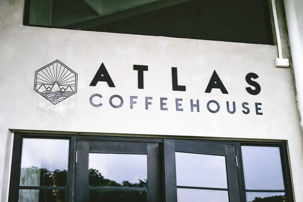 Close-up of the Atlas Coffeehouse sign and logo on a white wall above a window.