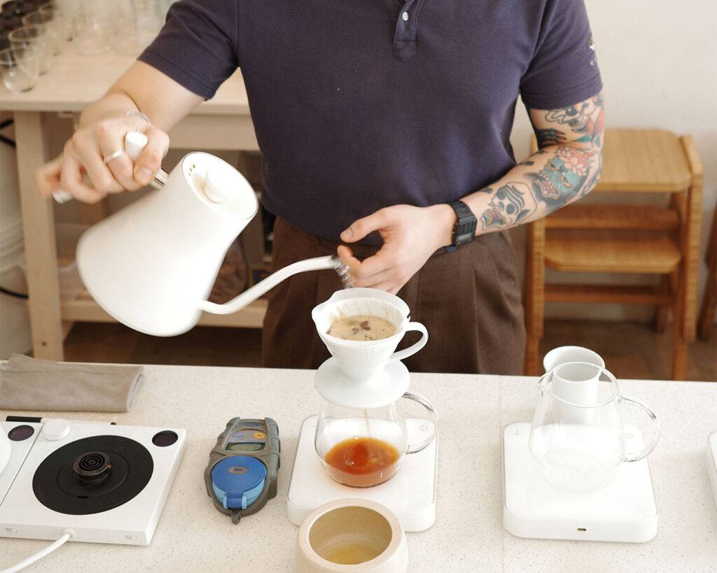 A barista carefully pours hot water over freshly ground coffee, capturing the calm ritual of manual brewing and the artistry behind every cup.