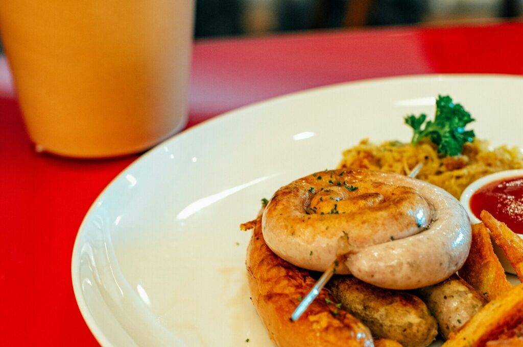 A plate featuring a sausage, crispy fries, and a side of ketchup, served as part of a Singapore brunch.