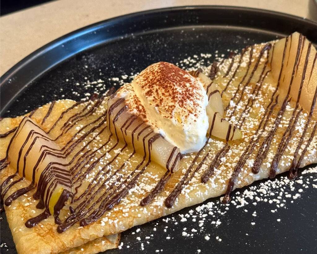 Soft, thin crêpes folded gently and finished with a smooth chocolate drizzle, offering a simple yet indulgent dessert experience.