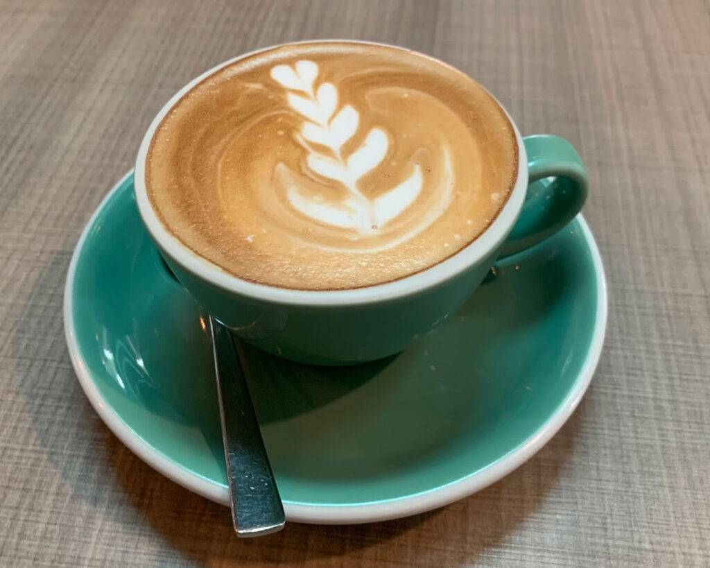A cup of coffee crowned with delicate latte art, resting on a wooden table and inviting a quiet moment of appreciation before the first sip.