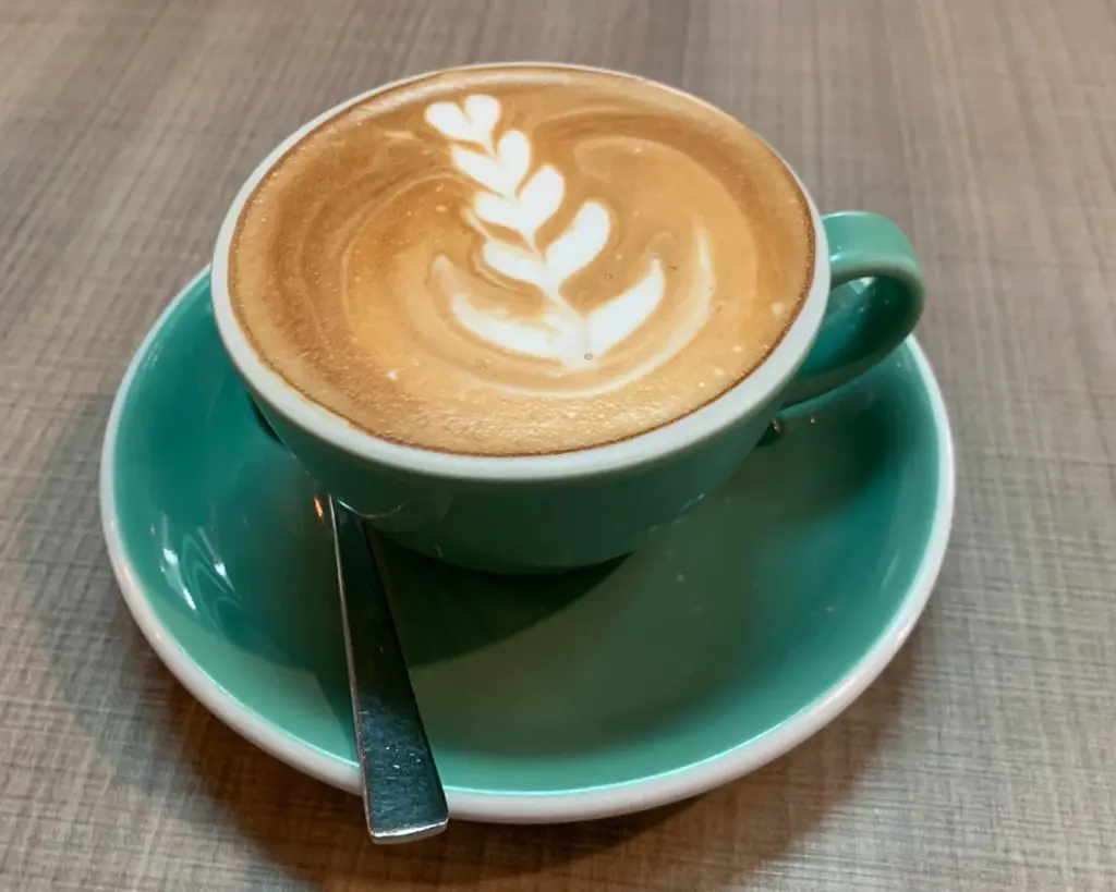 A cup of coffee crowned with delicate latte art, resting on a wooden table and inviting a quiet moment of appreciation before the first sip.