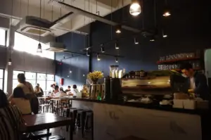 Interior view of a modern, industrial-style cafe in Singapore, featuring a marble-topped counter, baristas working with professional coffee machines, and patrons seated in a cozy, dimly lit dining area.