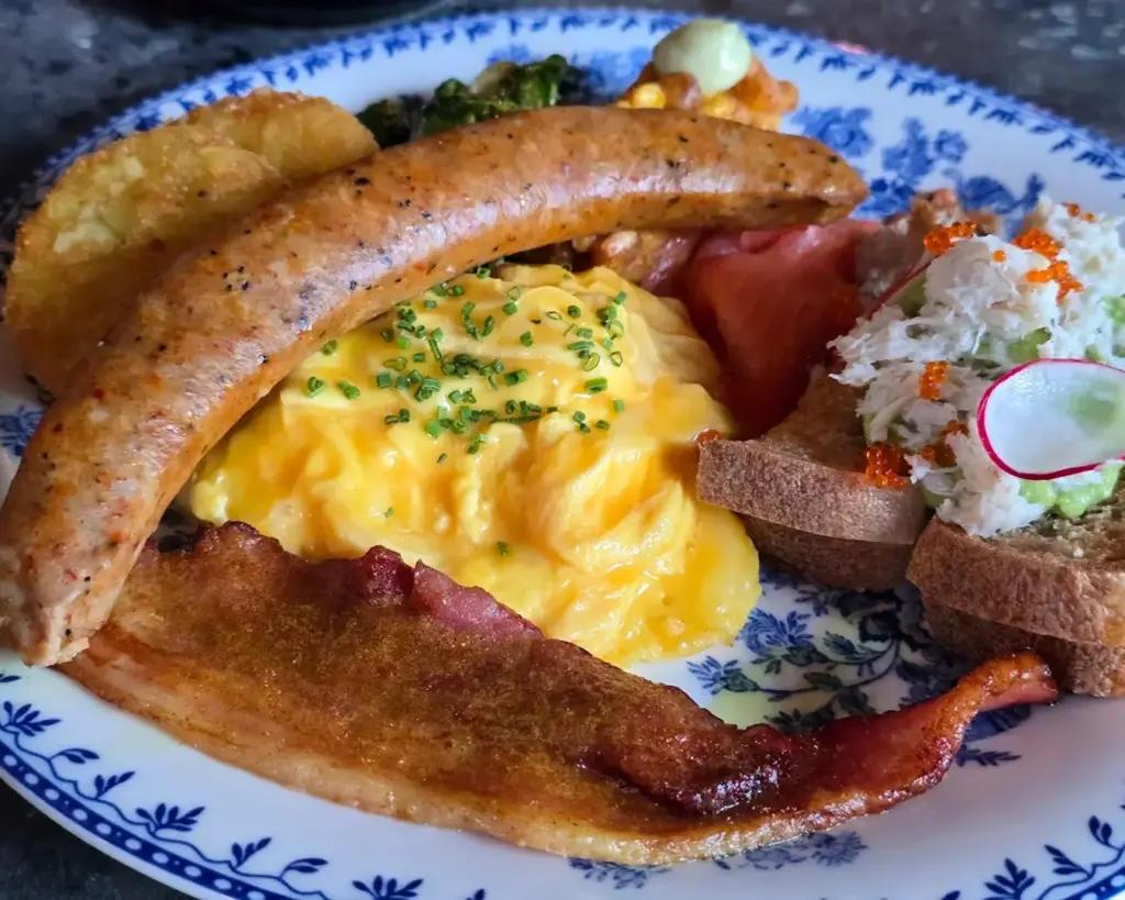 A hearty breakfast plate featuring juicy sausages, fluffy scrambled eggs, crispy hash browns, and strips of golden-brown bacon, served warm and freshly cooked.