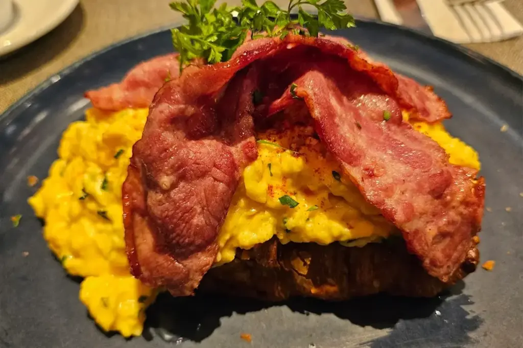 Toast topped with creamy, softly scrambled eggs and crispy bacon, creating a rich and satisfying contrast of textures, served at Populus.
