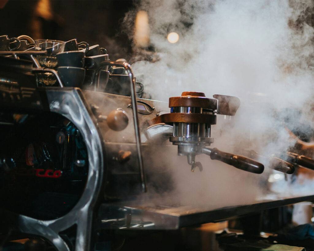 A sleek espresso machine with steaming hot water pouring into a cup, highlighting the professional setup of a café.