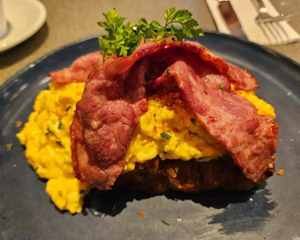 Toast topped with creamy, softly scrambled eggs and crispy bacon, creating a rich and satisfying contrast of textures