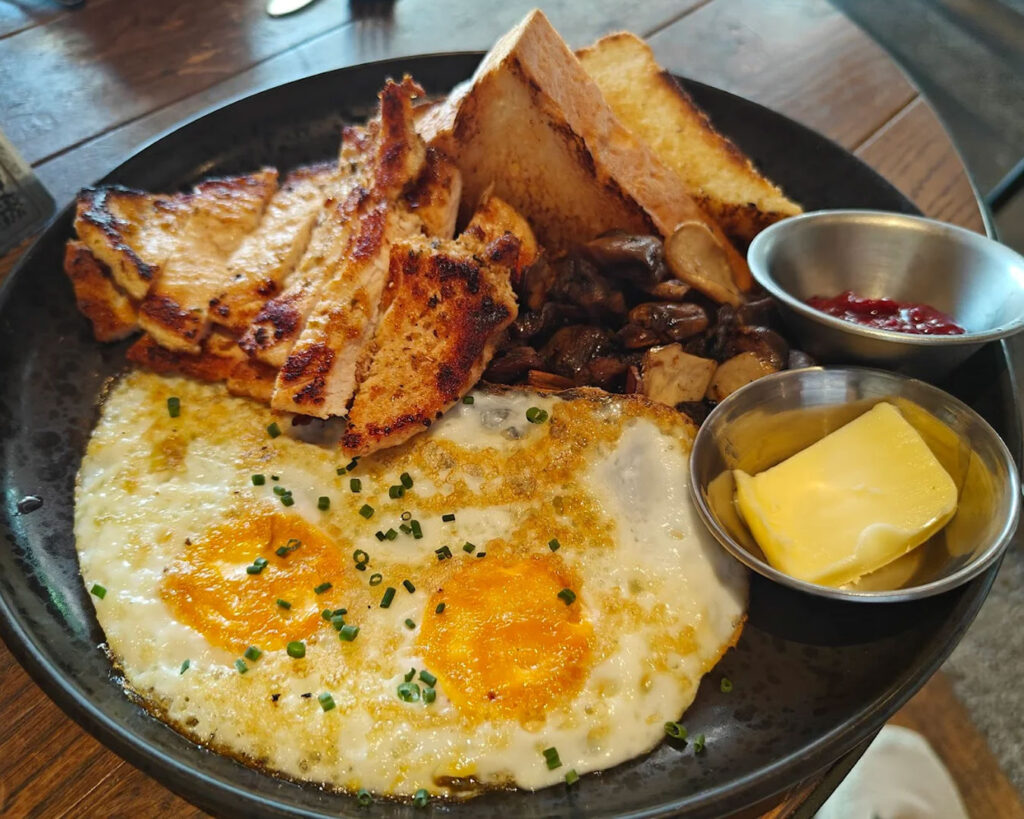 A savoury grilled chicken dish topped with a perfectly cooked egg, plated neatly and served hot, showcasing a hearty café-style meal with rich textures and appetising colours.