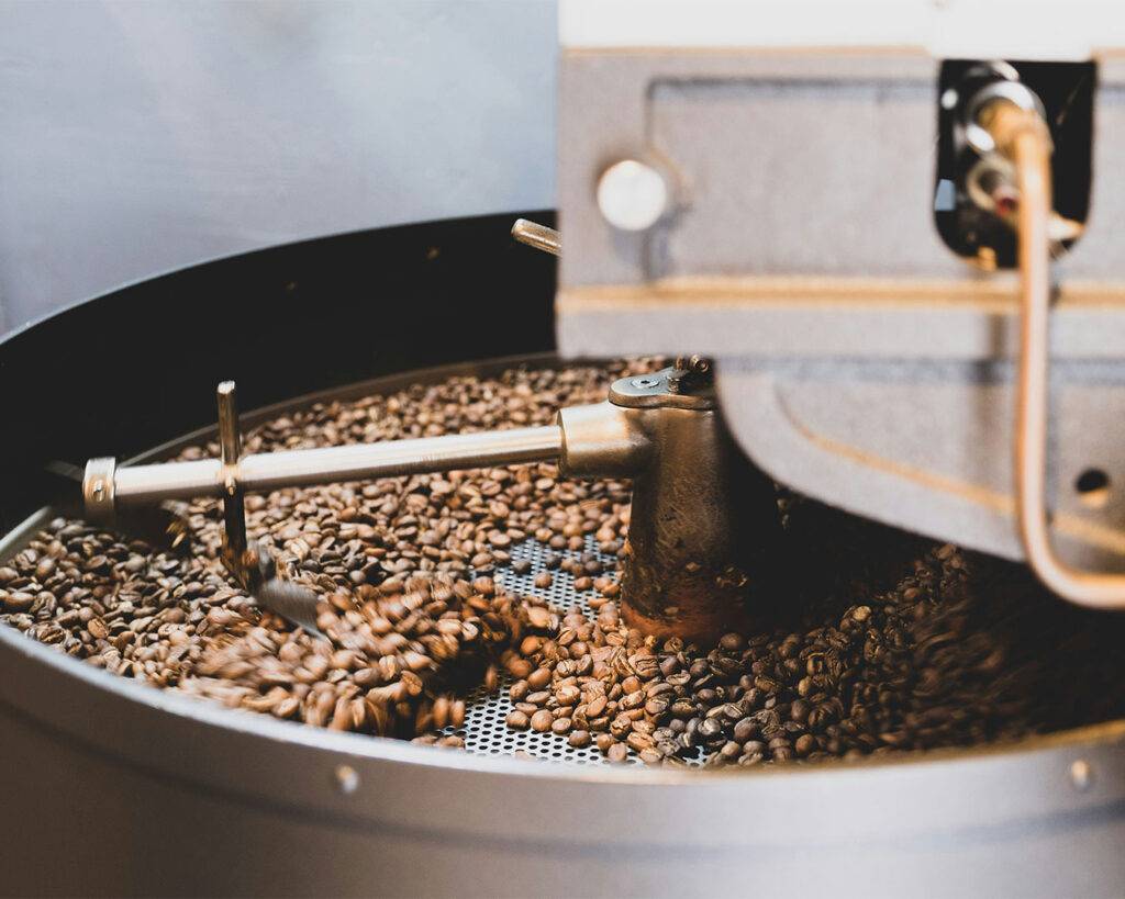 Coffee beans being roasted in a drum roaster, with a warm golden-brown glow indicating the beans reaching the perfect roast.