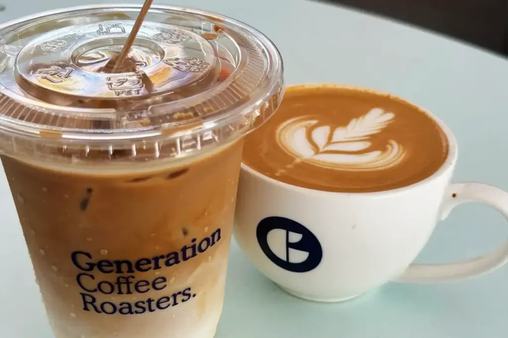A glass and a cup of Generation coffee placed side by side, showcasing a cosy café setting with freshly brewed drinks ready to enjoy.