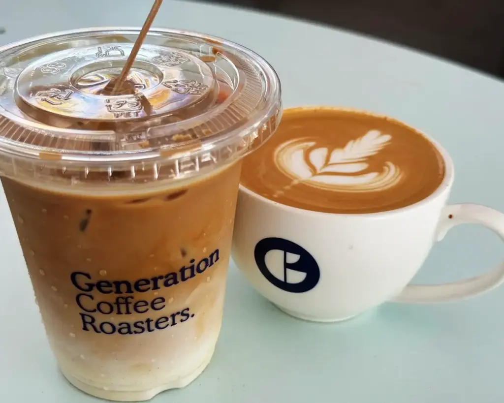 A glass and a cup of Generation coffee placed side by side, showcasing a cosy café setting with freshly brewed drinks ready to enjoy.