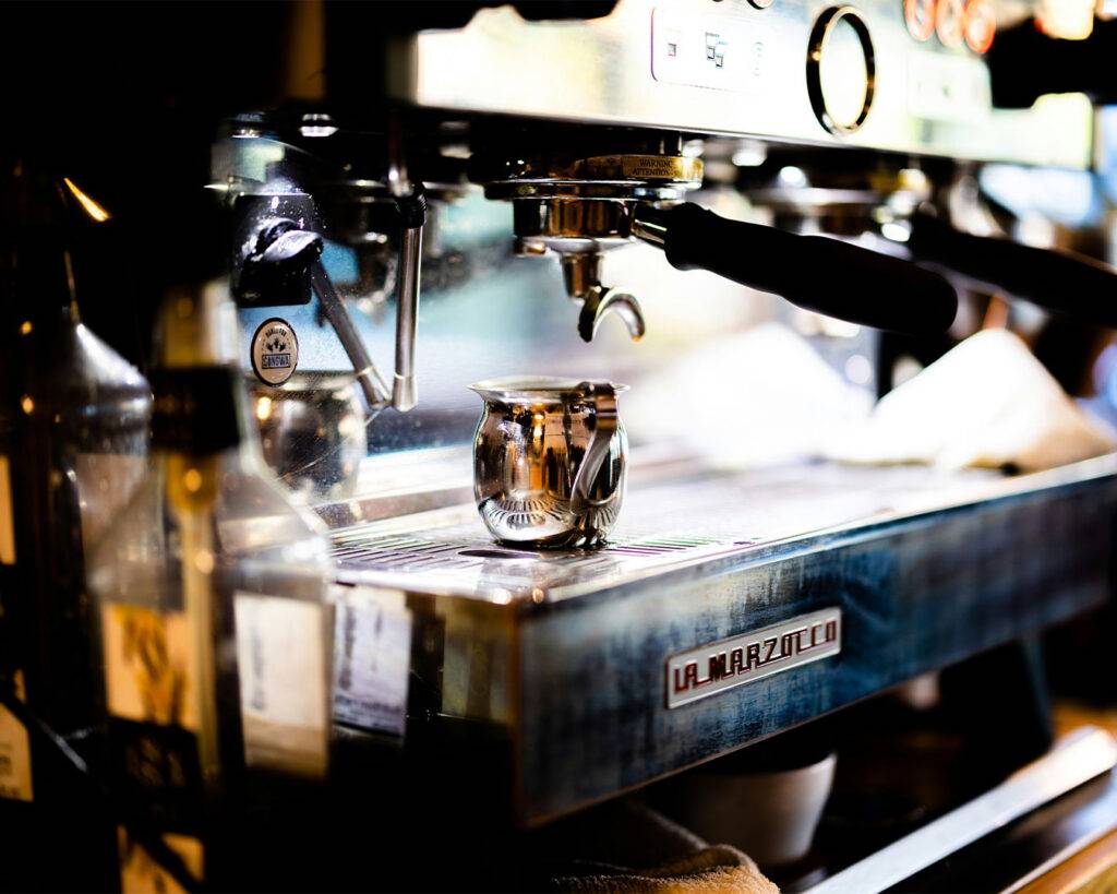 A professional espresso machine on a café counter, with metal surfaces and control buttons visible, ready for preparing fresh espresso shots.