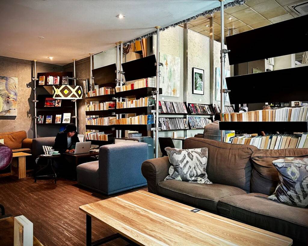 A charming café exterior along Robertson Quay, featuring warm lighting and a welcoming entrance that blends literary charm with a peaceful riverside setting.