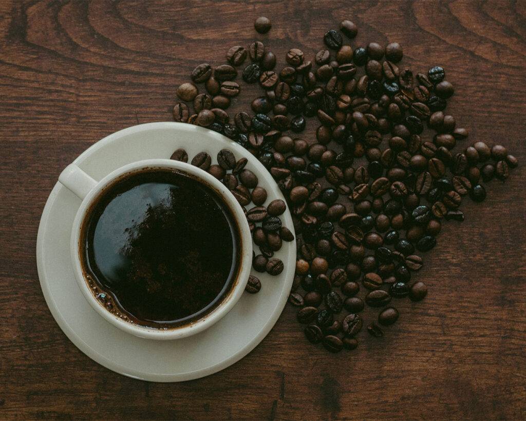 A ceramic cup of coffee placed next to a pile of coffee beans on a wooden table, highlighting the connection between raw beans and the finished drink.