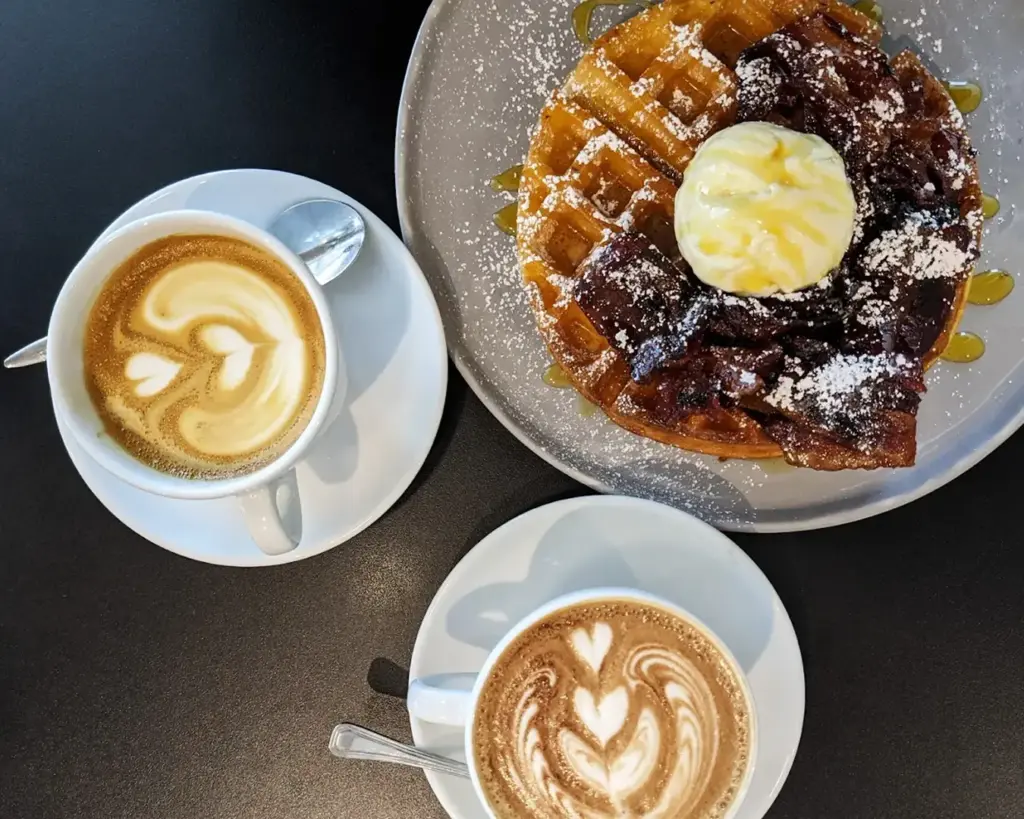 Two cups of coffee served alongside a waffle topped with a scoop of ice cream, blending warm and cold elements for a delightful dessert-style treat.