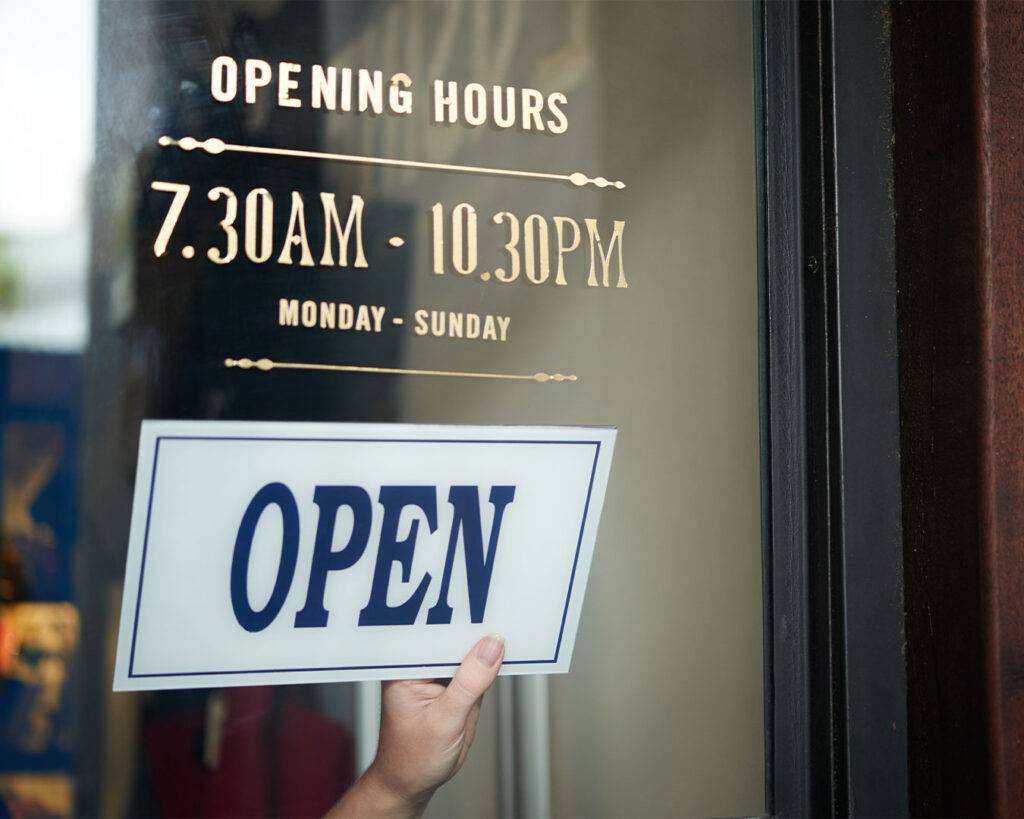 An “Open” sign hanging on a glass café door, welcoming customers inside during business hours.