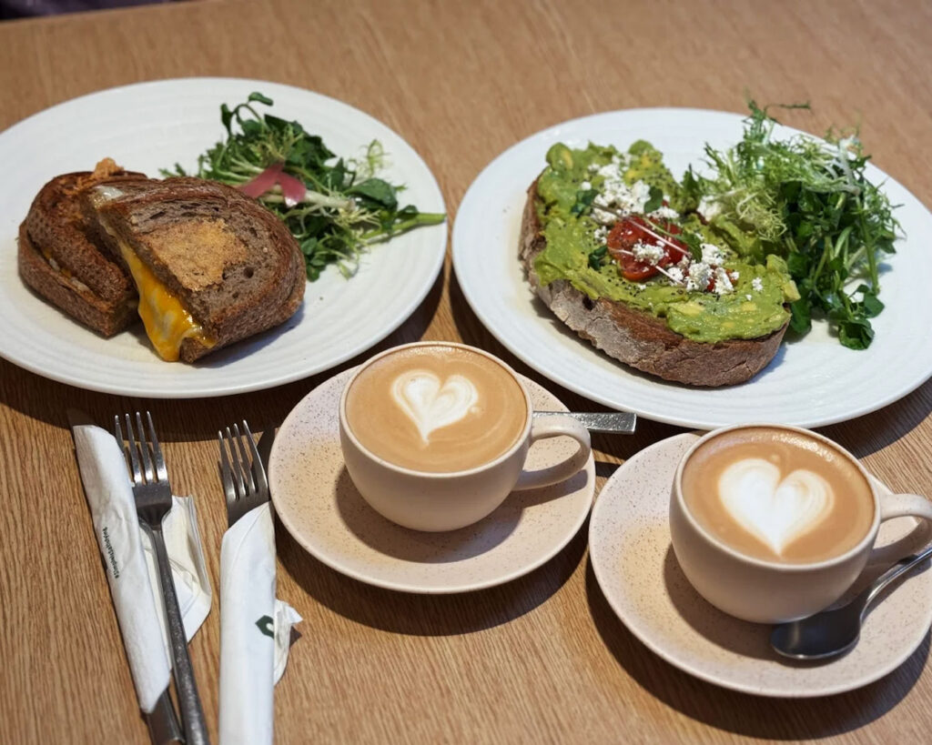 A cup of coffee paired with a sourdough-based dish on a café table, styled simply to emphasise the contrast between the warm beverage and the freshly prepared food.
