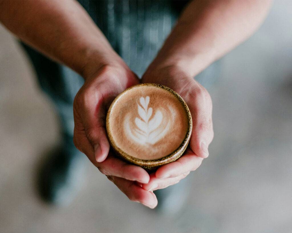 Close-up of a beautifully presented cup of latte with detailed latte art, held carefully in the barista’s hand, ready to serve.