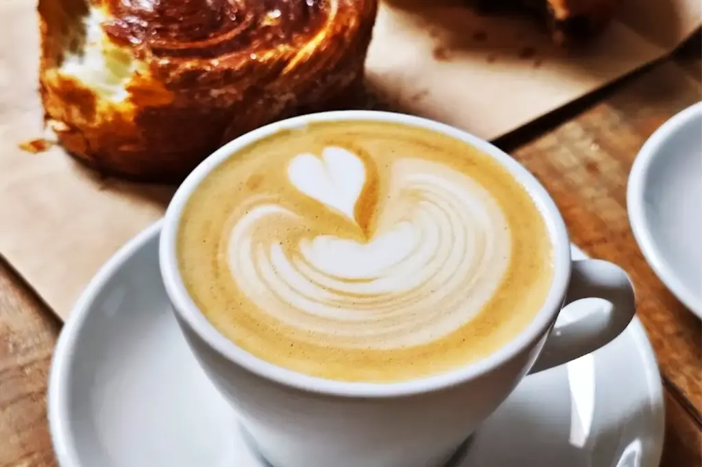 A cup of coffee with intricate latte art on top, paired with an assortment of pastries, creating a warm and inviting café scene at Nylon Coffee Roasters.