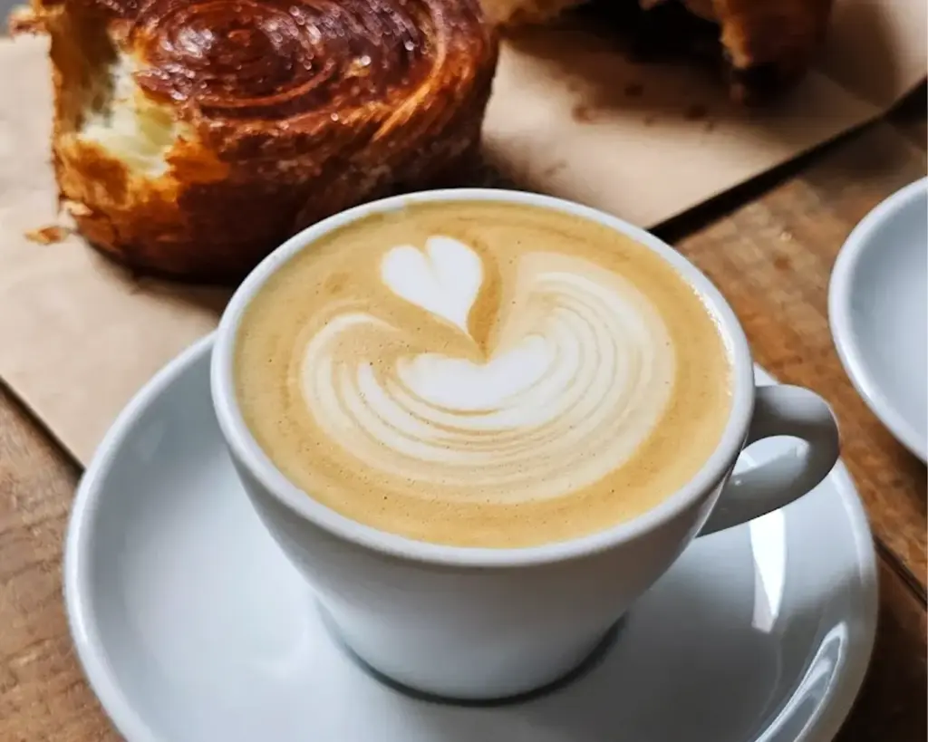 A cup of coffee with intricate latte art on top, paired with an assortment of pastries, creating a warm and inviting café scene.