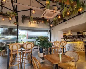 A cosy garden café interior filled with natural light, featuring wooden furniture, lush greenery, and soft earthy tones that create a calm, relaxing atmosphere—perfect for a quiet coffee break or casual