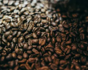 A close-up of whole coffee beans scattered across a textured surface, showcasing their rich brown tones and natural oils, highlighting their freshness and origin.